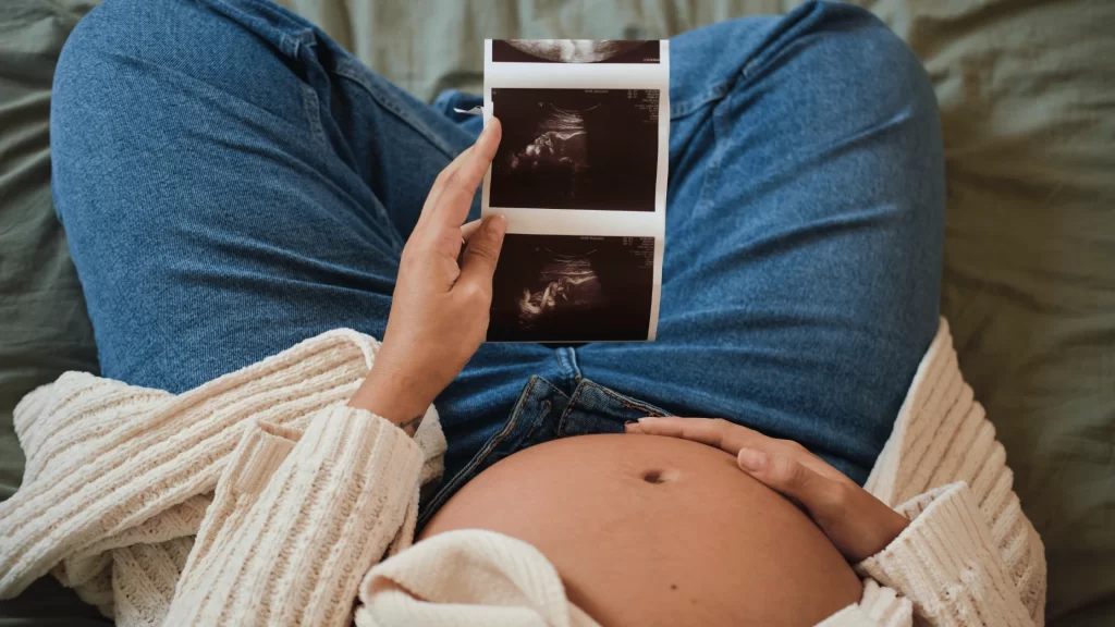 Pregnant surrogate holding ultrasound images while considering questions to ask a surrogacy agency